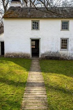 Idyllic path leads through grass to open door of whitewashed stone cottage Stock Photos