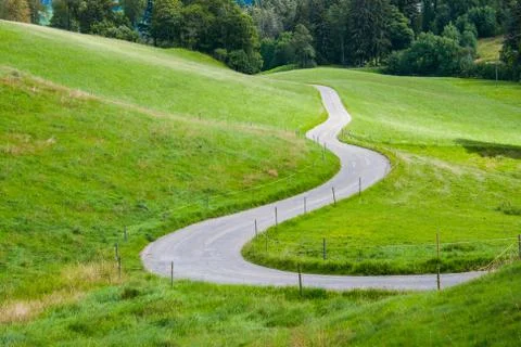 Idyllic road between green fields in the mountains Stock Photos