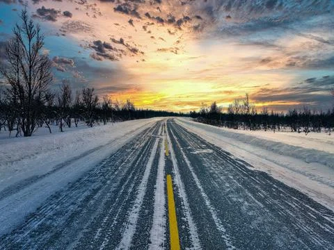 Idyllic winter scene featuring a long and desolate road surrounded by a forest Stockfoto's