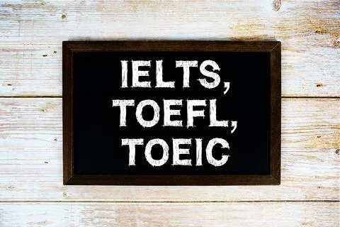 IELTS, TOEFL, TOEIC text with gift box present and alarm clock on black bac.. Stock Photos