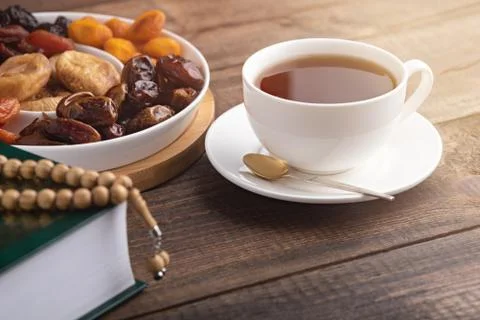 Iftar concept, white Cup of tea, plate of dried fruit, Koran with prayer bead Stock Photos
