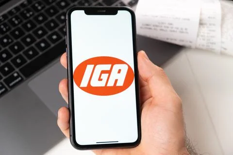 IGA application on the screen of Apple iPhone in mans hand and laptop on the Stock Photos