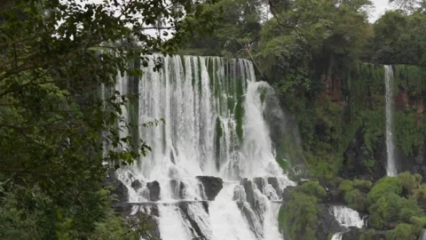 Iguazu waterfall cascading down cliffs framed by green jungle foliage in slow 스톡 동영상 345037896