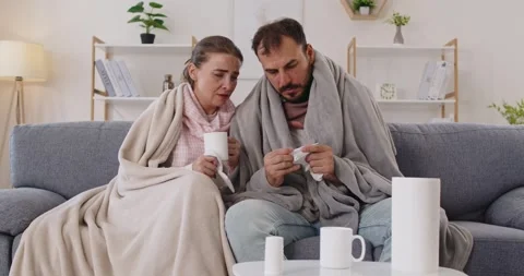 Ill couple on sofa, wrapped in blankets, checking tissues and planning medicine Stock Footage 324867763