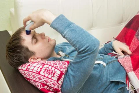 Ill man checking temperature, lying on sofa Stock Photos