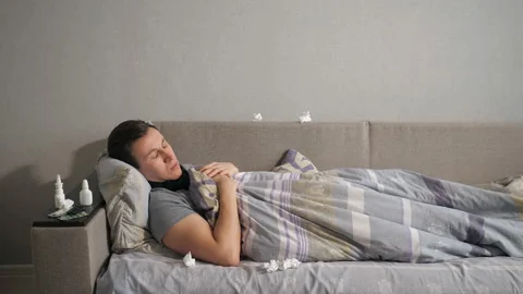 Ill man with flu and runny nose wipe his nose with a tissue while lying on couch Stock Footage 101232339