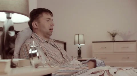 Ill man sitting in bed wipes nose in tissue Видео 68420962
