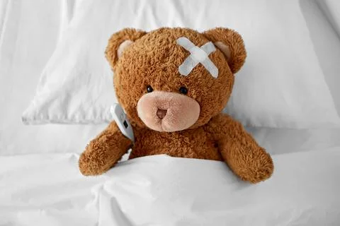 Ill teddy bear with patch and thermometer in bed Foto stock