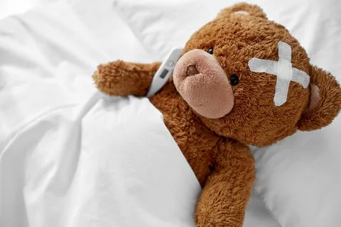Ill teddy bear with patch and thermometer in bed Foto stock