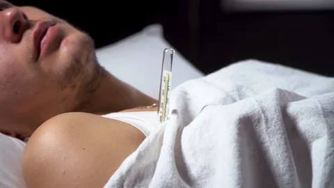 Ill young man is taking temperature and coughing in his bed Stock Footage 125809771