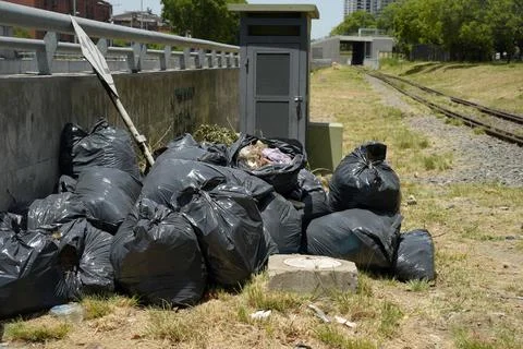 Illegal Dumping of Black Garbage Bags Near Urban Railway Stock Photos