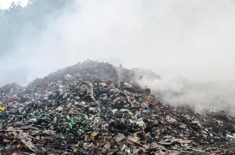 Illegal waste dump. Piles of garbage in nature. Burning open landfill site Stock Photos