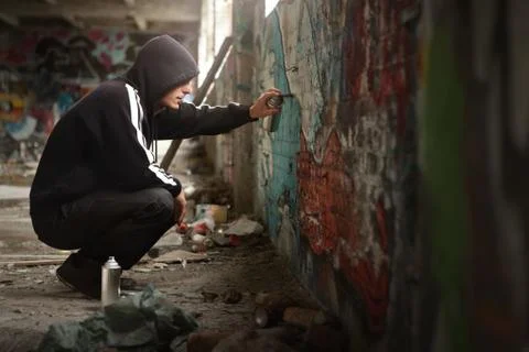 Illegal young man spraying paint on a graffiti wall. Stock Photos