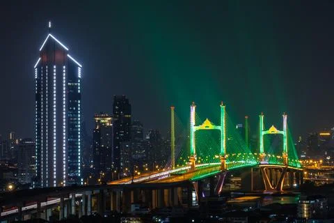 Illuminated Cable-stayed Bridge And Modern Skyscraper Towering Over Chao Ph.. Photos