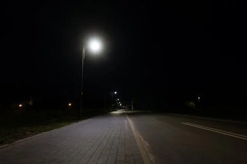 Illuminated empty sidewalk and asphalt street in suburbs Foto stock