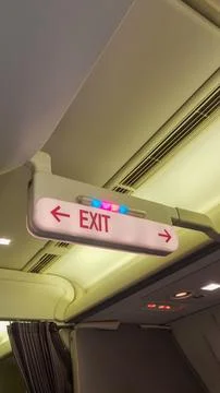 Illuminated exit sign inside a commercial aircraft cabin featuring colorful MCLP Stock Photos