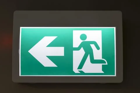 Illuminated green exit sign featuring a running figure and left-pointing arro Stock Photos
