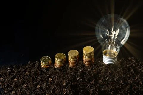 Illuminated light bulb with coins stack Foto stock
