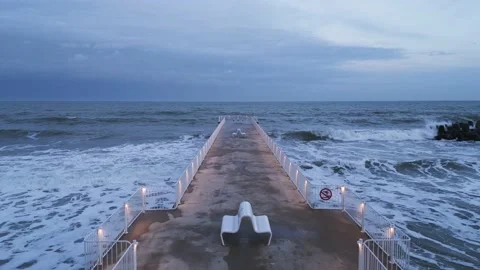 Illuminated pier with dramatic sky over stormy dark sea at evening, Varna Stock Footage 231684883