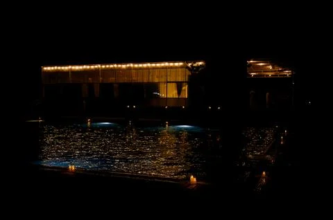 Illuminated poolside building at night with reflections on water surface Stock Photos