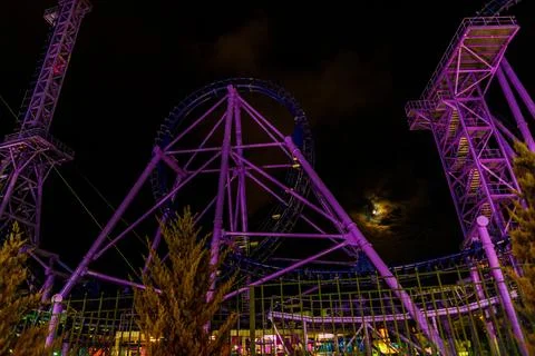 Illuminated purple roller coaster structure at night under a full moon Stock Photos