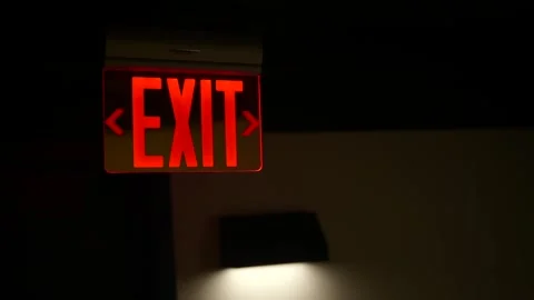 Illuminated red exit sign with directional arrows in a dimly lit interior space Stock Footage 345442800