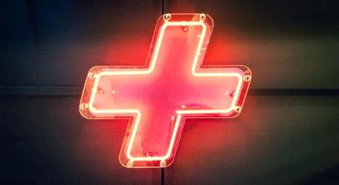 Illuminated red neon light, plus symbol on the wall Stock Photos