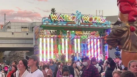 Illuminated retro neon lights carnival games waterworks with large crowds Stock Footage