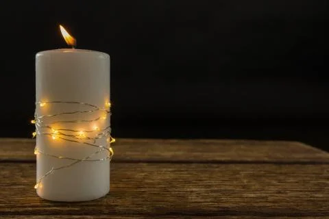 Illuminated string lights wrapped on lit candle Stock Photos