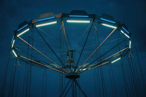 Illuminated swing carousel structure at dusk with glowing neon lights again.. Stock Photos