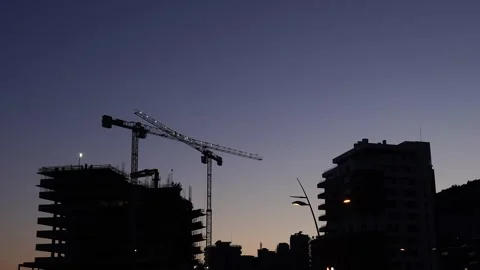 Illuminated tower cranes stand on a construction site against the sunset sky Stock Footage 268943914