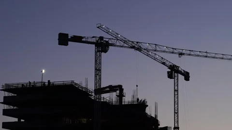 Illuminated tower cranes work at a construction site against a purple darkening Stock Footage 270312768