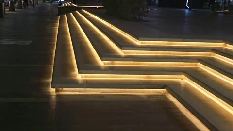 Illuminated zig-zag steps with warm LED strip lighting in a modern public plaza. Stock Footage 341364963