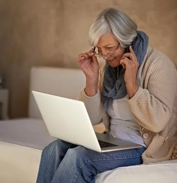 Im checking my emails now...A senior woman on her mobile while using her laptop 写真素材