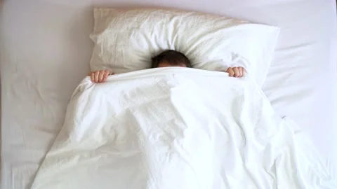 Image from above of young man hiding behind bed linens during the morning. Stock Footage 132184656