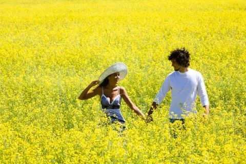 Image of amorous couple walking in yellow meadow holding by hands and looking at Stock Photos