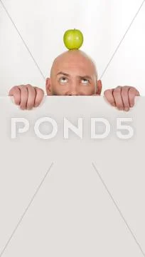 Image of annoyed man looking at apple on his bald head Stock Photos