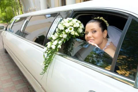 Image of beautiful bride showing her rose bouquet out of wedding limousine and l Stock Photos