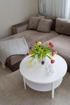 Image of beige soft sofa with white round wooden table and colourful tulips Foto stock