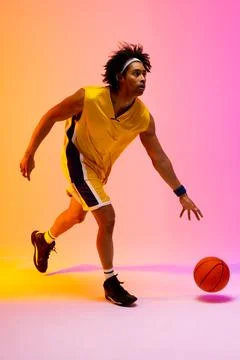Image of biracial basketball player bouncing basketball on pink to orange Stock Photos