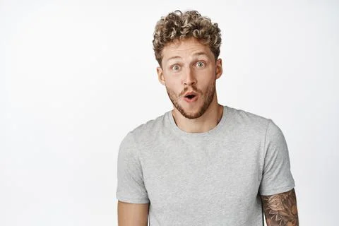 Image of blond young man looking surprised, amazed by something cool, checking Stock Photos