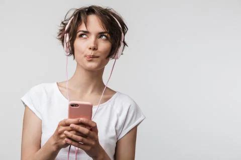 Image of brooding woman in basic t-shirt holding smartphone while listening t Stock Photos