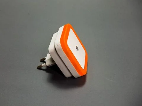 The image captures a modern, angular white and orange nightlight on a grey .. Stock Photos