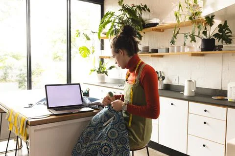 Image of caucasian non-binary trans woman with laptop working in sewing workshop Stock Photos