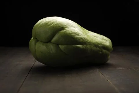 Image of a chayote fruit close up on rustic wooden surface and black backgrou Stock Photos