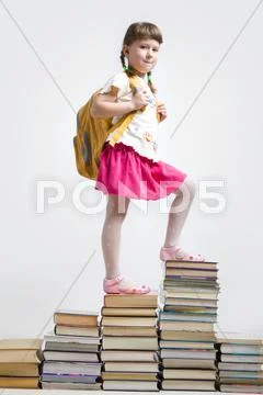 Image of clever girl with backpack standing on heap of books Stock Photos