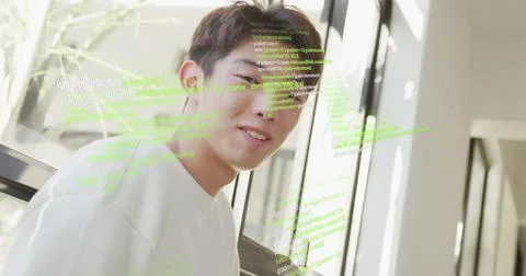 Image of computer language over smiling asian man sitting on chair at home Foto stock