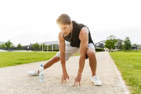 Image of concentrated man working out with earphones and running at green par 스톡 사진