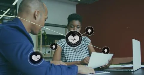 Image of connected icons over diverse coworkers discussing reports on desk in Stock Photos