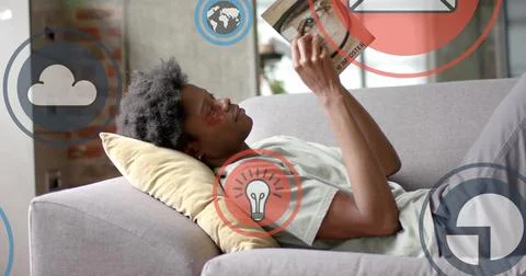 Image of data processing over african american man reading book on sofa Foto stock